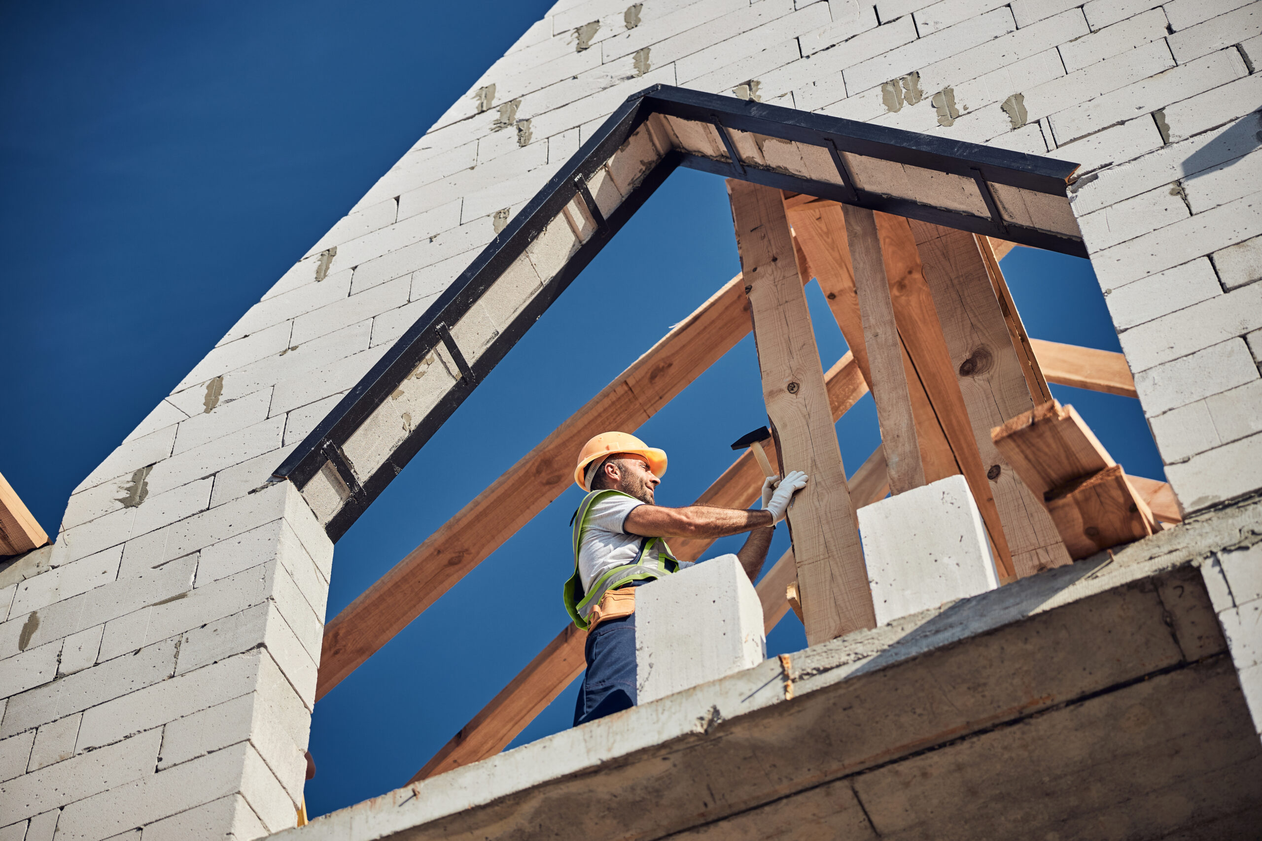 Construction worker wearing orange hardhat and hitting a nail with a hammer while building a house